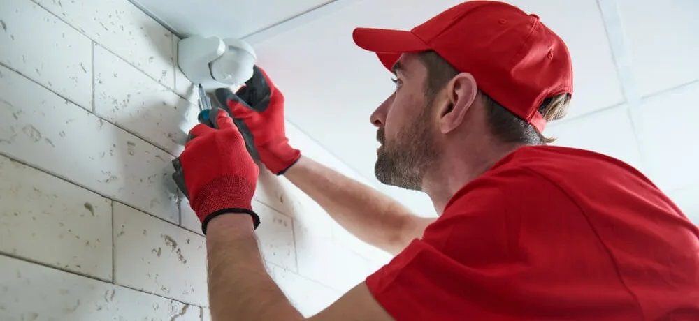 Profissional com roupas vermelhas instalando um sensor de presença