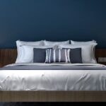 Imagem de um quarto com parede azul marinho e cama de casal com lençol branco