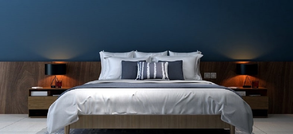 Imagem de um quarto com parede azul marinho e cama de casal com lençol branco