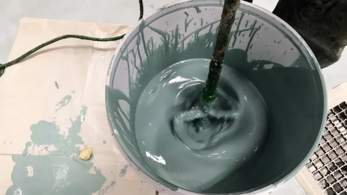 Imagem mostra um balde com tinta verde sendo misturada