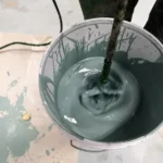 Imagem mostra um balde com tinta verde sendo misturada