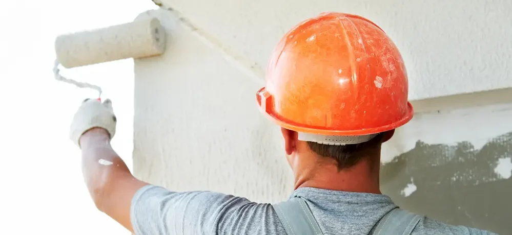 Imagem de um homem pintando uma parede com um rolo de tinta.