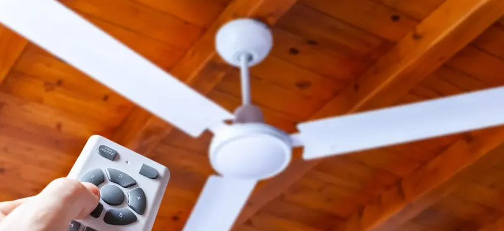 Pessoa usando um controle remoto para ligar ou ajustar um ventilador de teto.