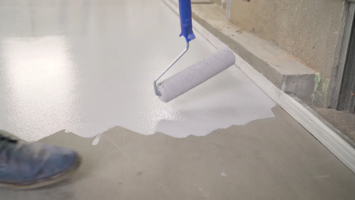 Imagem de um rolo de pintura aplicando tinta branca no chão de cimento.