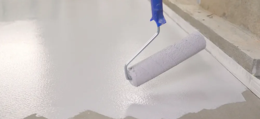 Imagem de um rolo de pintura aplicando tinta branca no chão de cimento.