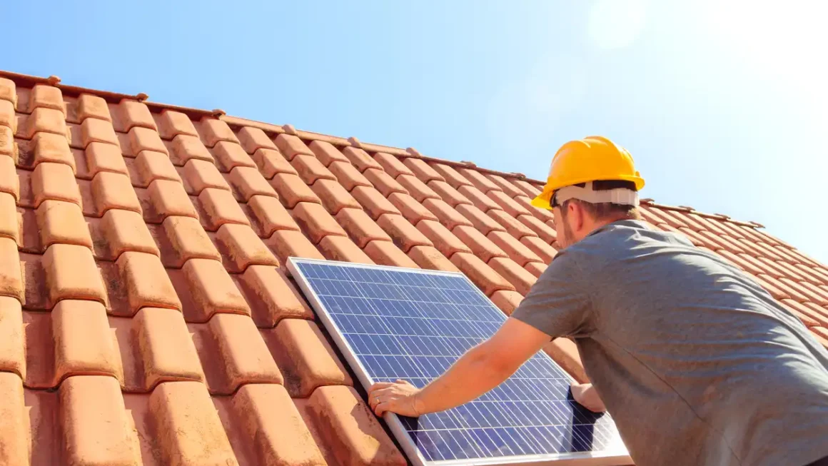 Imagem de um homem instalando um painel solar sobre um telhado.