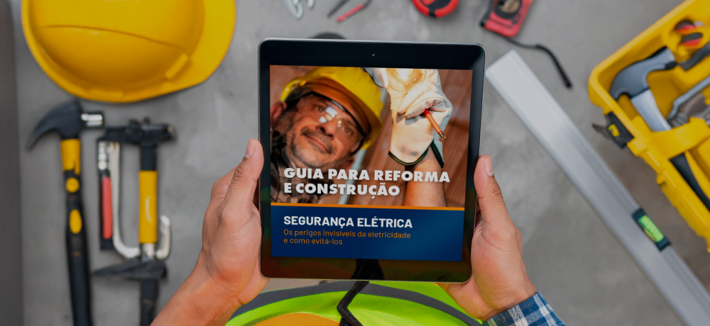 Pessoa segurando tablet com a capa do Guia para Reforma e Construção da Obramax sobre segurança elétrica