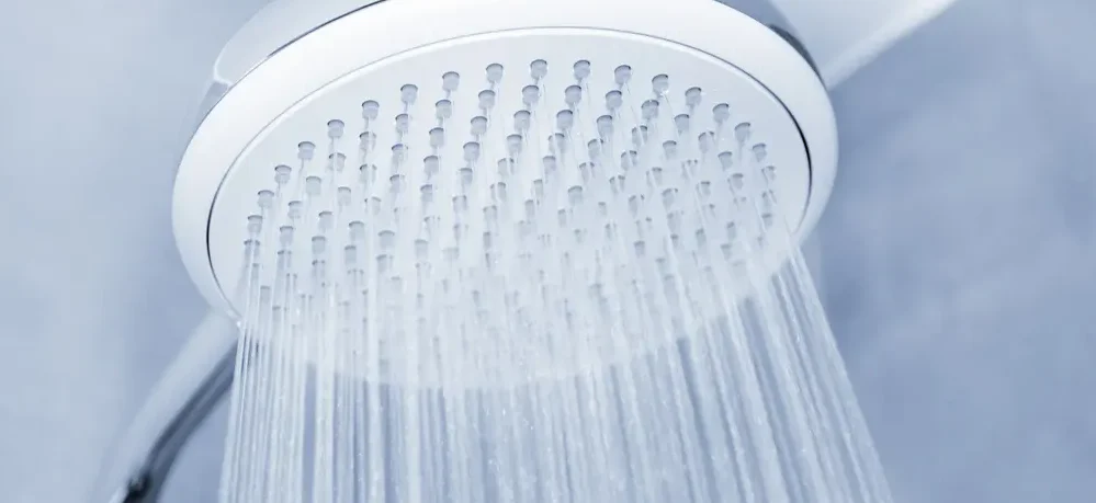 Imagem de um chuveiro ligado com água caindo.