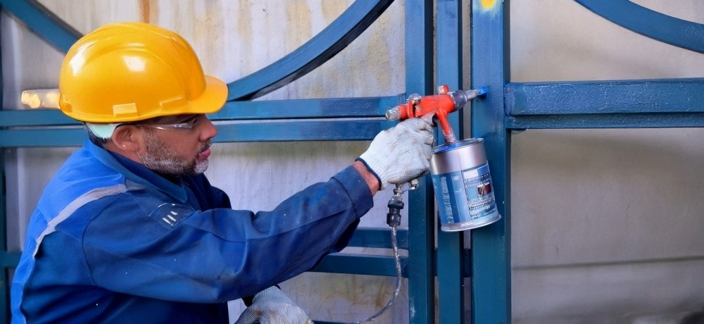 Profissional mostrando como funciona compressor de ar ao pintar um portão de ferro