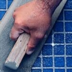 Profissional aplicando um rejunte para piscina com pastilhas na cor azul como uma desempenadeira