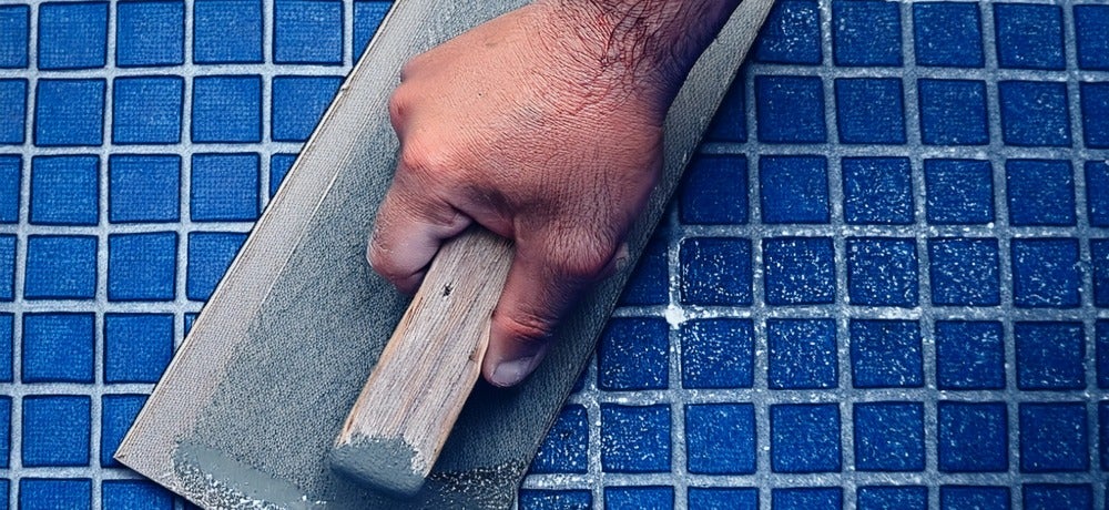 Profissional aplicando um rejunte para piscina com pastilhas na cor azul como uma desempenadeira