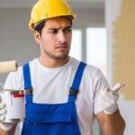 Pintor com rolo de pintura, pensando em como calcular quantidade de tinta para parede