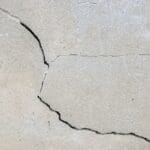 Rachadura na parede cinza de alvenaria, com sinais visíveis de trinca