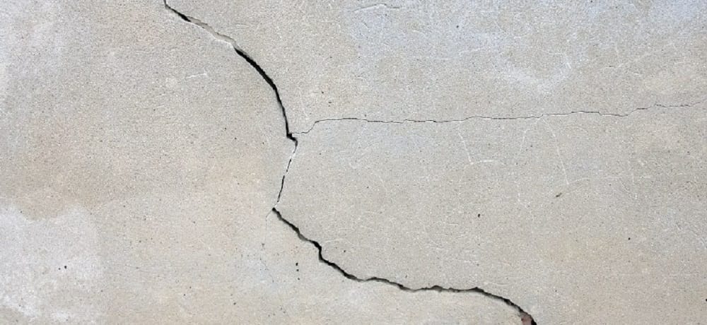 Rachadura na parede cinza de alvenaria, com sinais visíveis de trinca