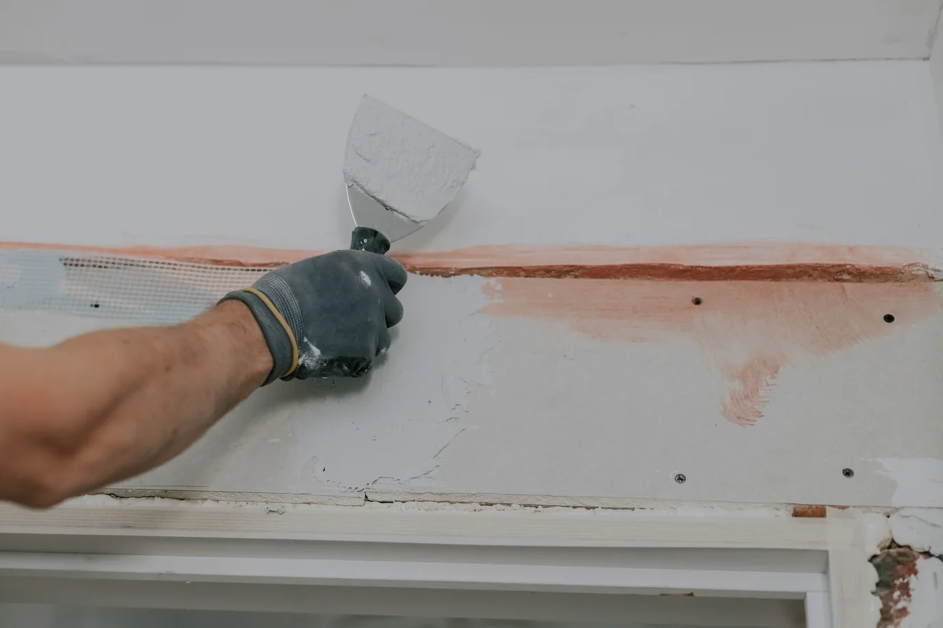 Profissional aplicando massa com espátula em parede de drywall após a remoção da tinta