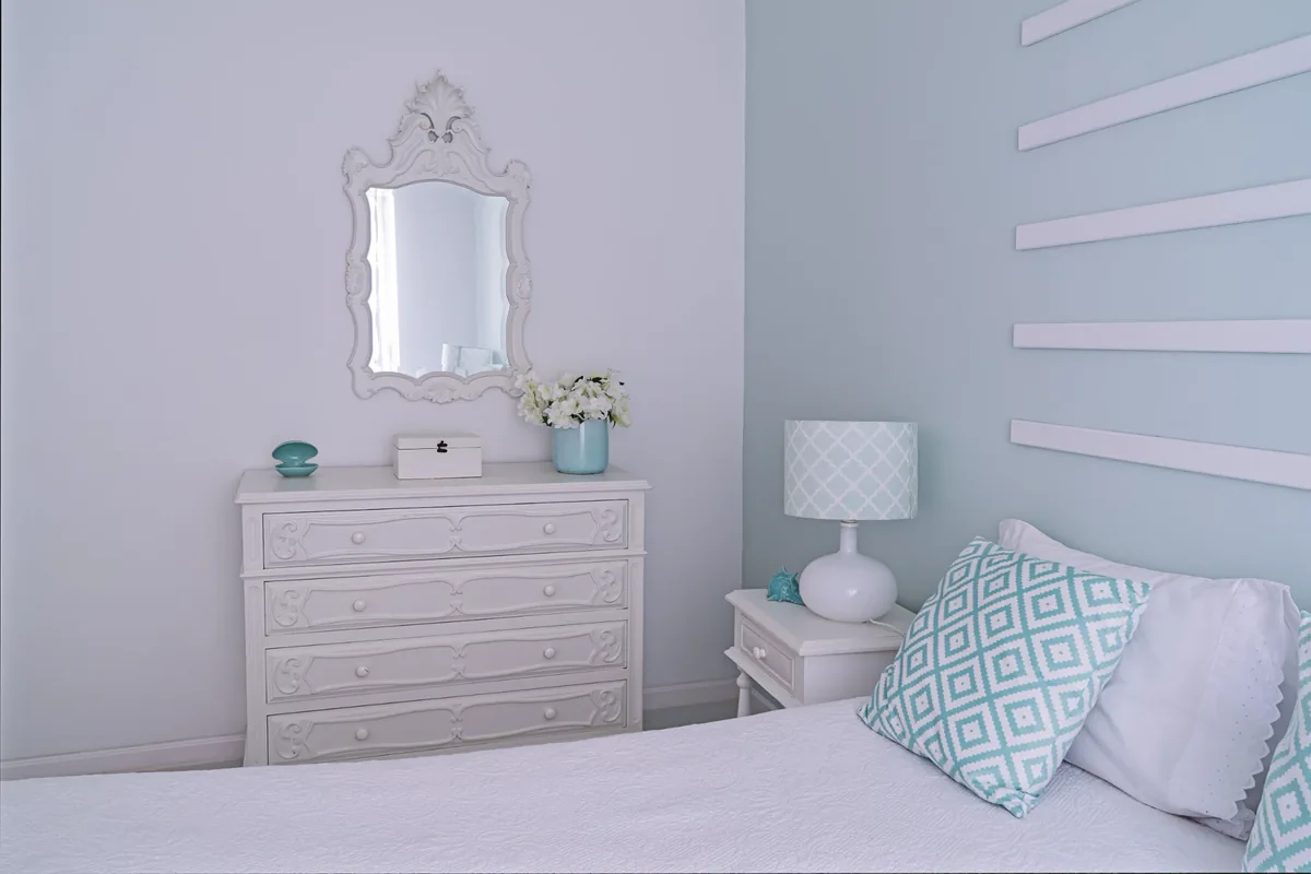 Quarto de casal com parede azul claro, cômoda branca e almofada estampada em tons de azul